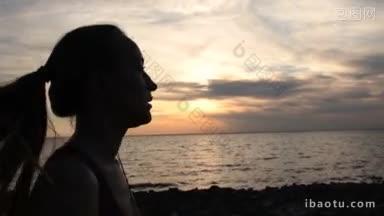 侧面的年轻迷人的女跑步者马尾辫在海边在日落时戴着耳机听音乐